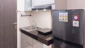 A compact kitchen with a built-in refrigerator, a sink, and a microwave. - Fully Furnished Studio With Mezzanine Bed At Serpong Garden Apartment (Cisauk)