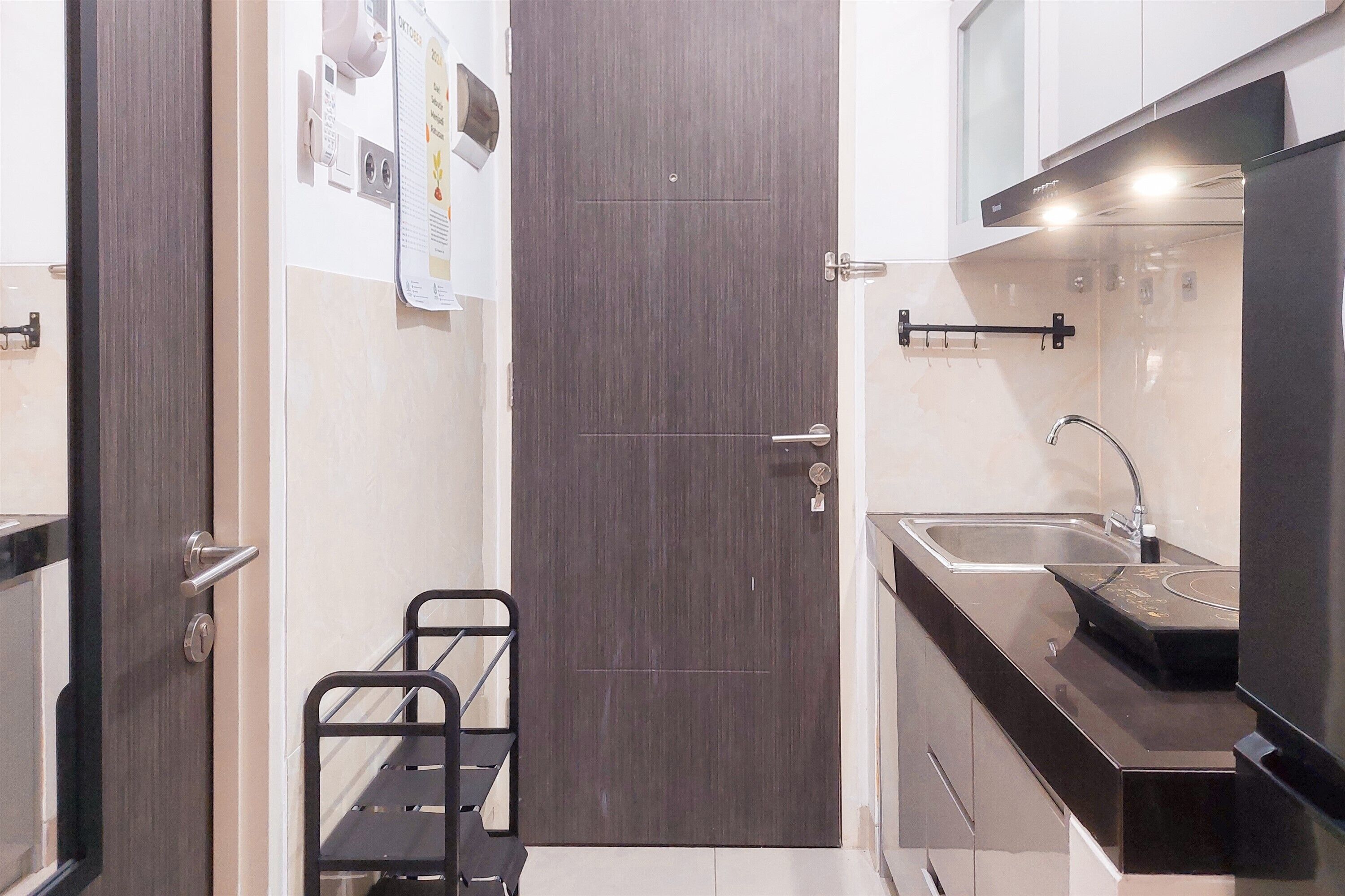 A compact kitchen with a dark wooden door, stainless steel sink, and a black countertop.
