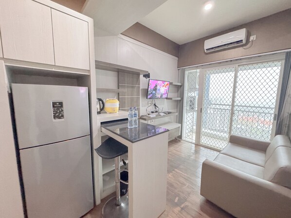 A modern kitchen with a built-in refrigerator, a coffee maker, and a water dispenser. There is a TV mounted on the wall and a sliding glass door leading to a balcony.