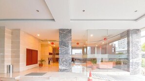 A modern lobby with a glass wall, a marble column, and a seating area with a plant. - Cozy Studio Apartment Mataram City (Ngaglik)