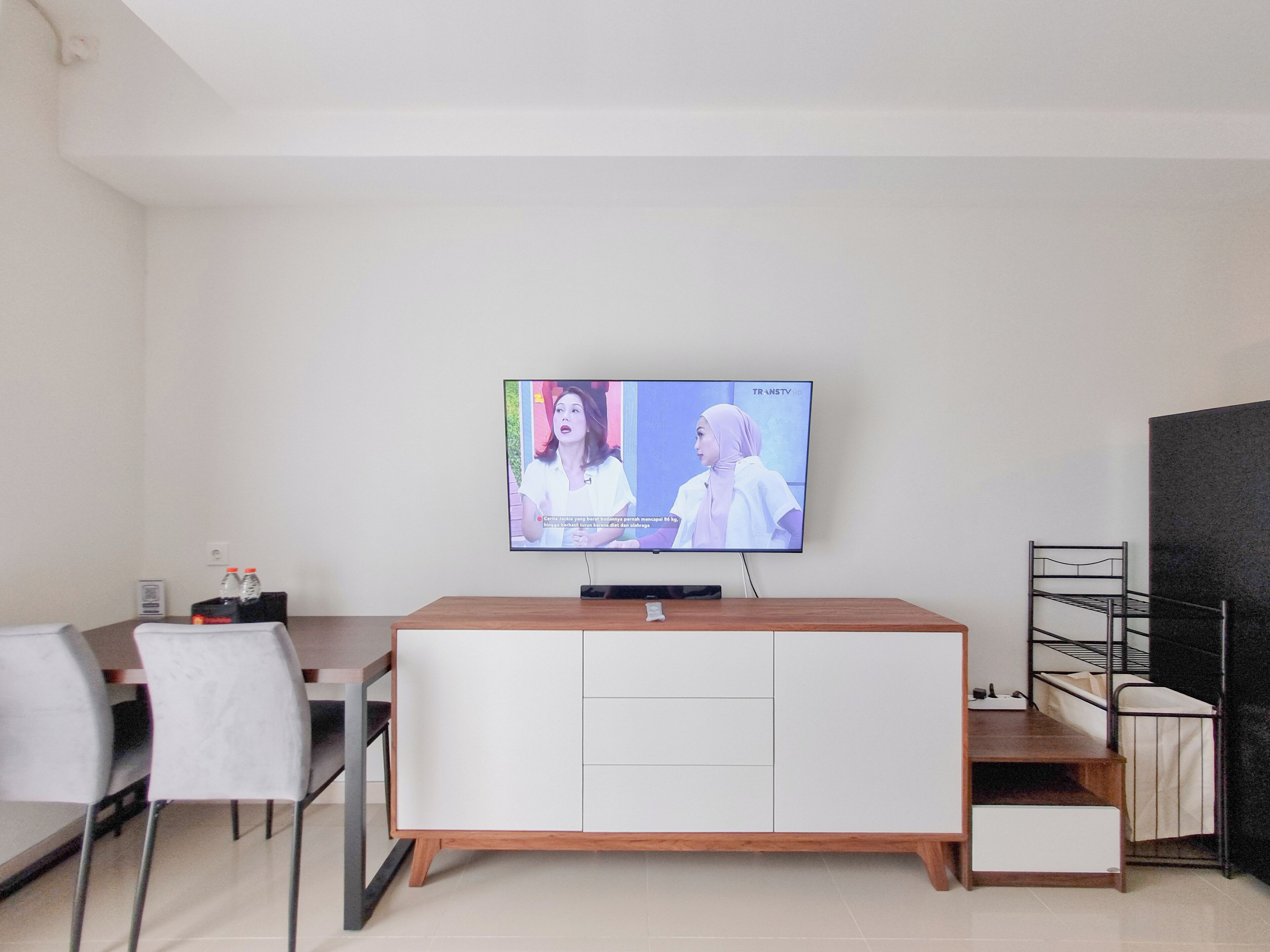A modern living room with a flat-screen TV mounted on the wall, a wooden cabinet, a metal shelf, and a white chair.
