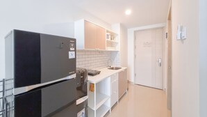 A compact kitchen with a black refrigerator, white cabinets, and a tiled backsplash. - Cozy Studio Apartment Mataram City (Ngaglik)