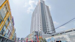 A tall, modern high-rise building with a grid of windows and balconies, surrounded by colorful buildings. - Spacious 3Br At Mekarwangi Square Cibaduyut Apartment (Bandung)