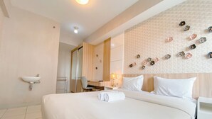 A hotel room with a large bed, a desk, a chair, a small table, a sink, and a mirror. - Spacious 3Br At Mekarwangi Square Cibaduyut Apartment (Bandung)