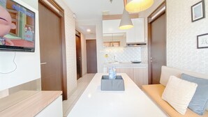 A modern living room with a TV, sofa, and a kitchen in the background. - Spacious 3Br At Mekarwangi Square Cibaduyut Apartment (Bandung)