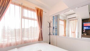 A hotel room with a bed, a coat rack, a window with curtains, and a television on the wall.