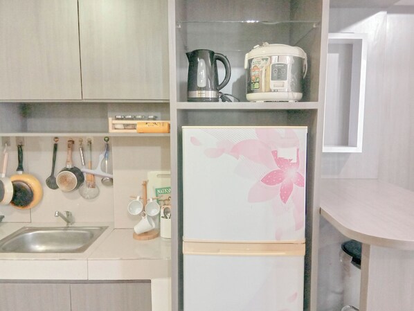 Una cocina con un lavamanos, una tetera, una cocedora de arroz y varios utensilios colgados en la pared.