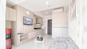 Ein modernes Wohnzimmer mit einer Couch, einem kleinen Tisch, einem Fernseher und einer Küchenzeile mit Kühlschrank und Mikrowelle.