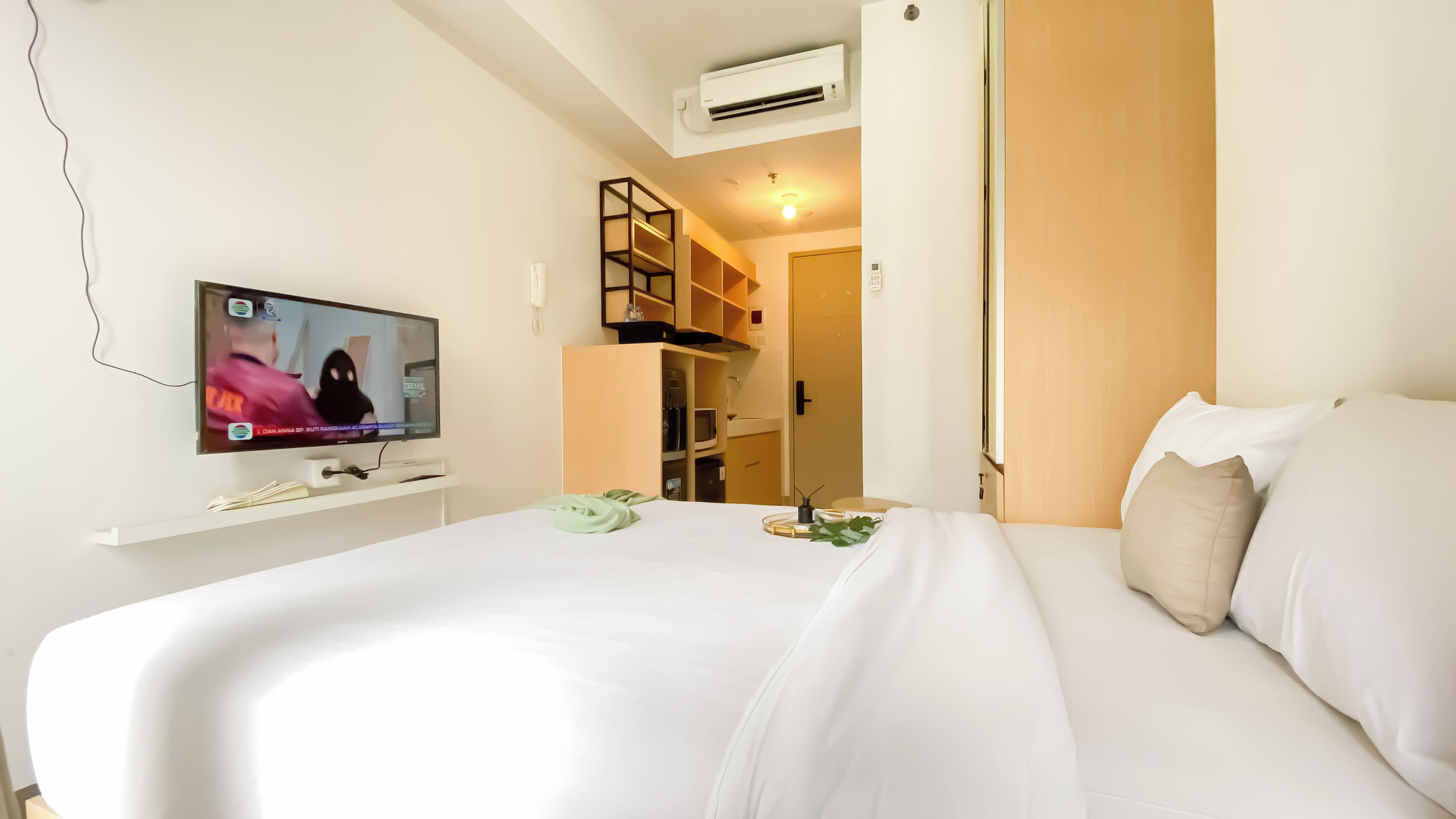 A hotel room with a bed, a TV, a wardrobe, and a small shelf with items.