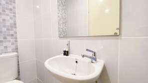 A bathroom with a white sink, a mirror, and a toilet. - Cozy Minimalist Studio Apartment Tokyo Riverside Pik 2 (Teluknaga)