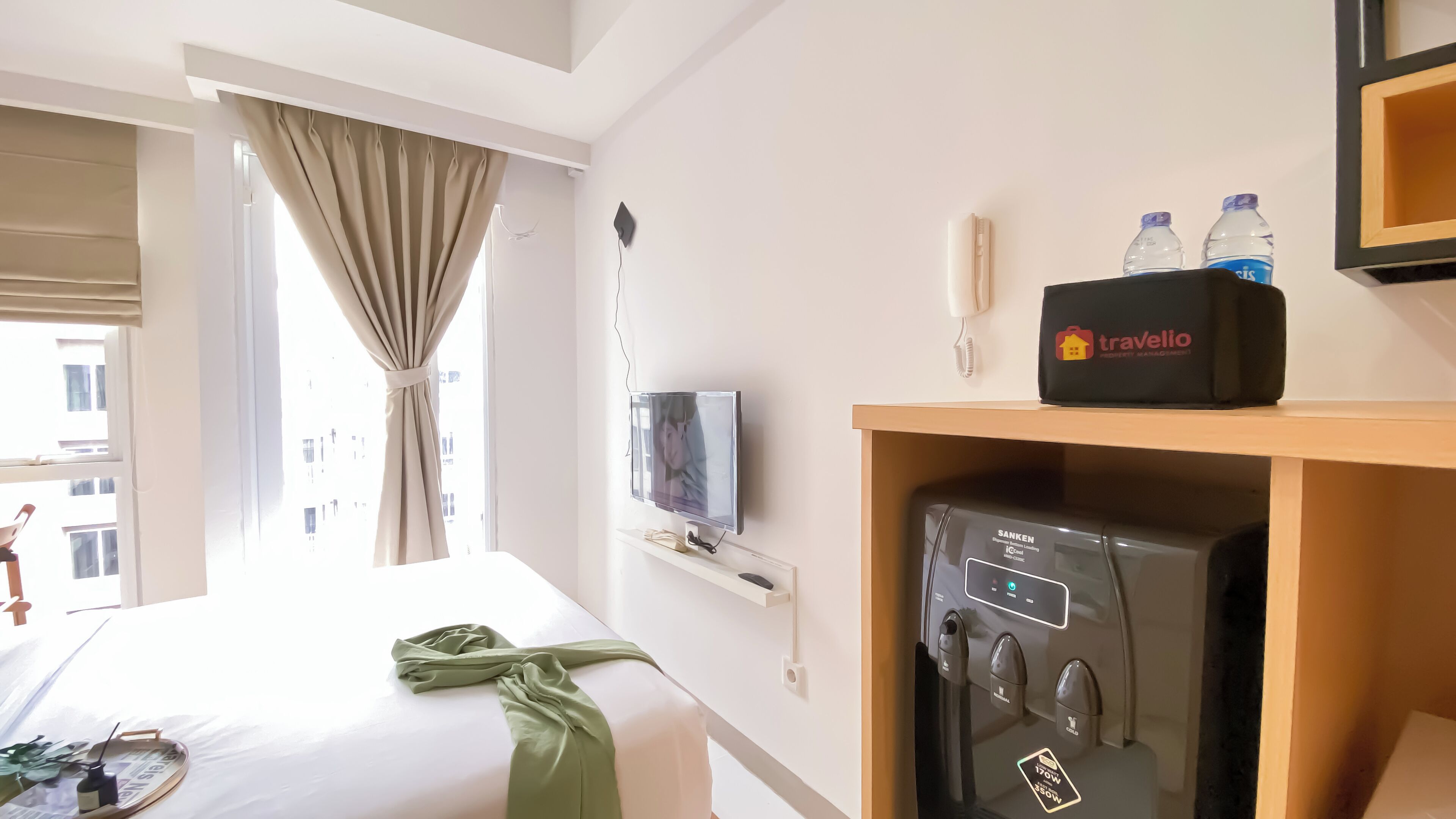 A hotel room with a bed, a TV, a minibar, and a view of the outside.