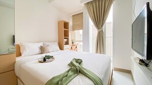 Una camera d'albergo con un letto grande, una TV, una finestra con tende e un tavolino con una pianta.