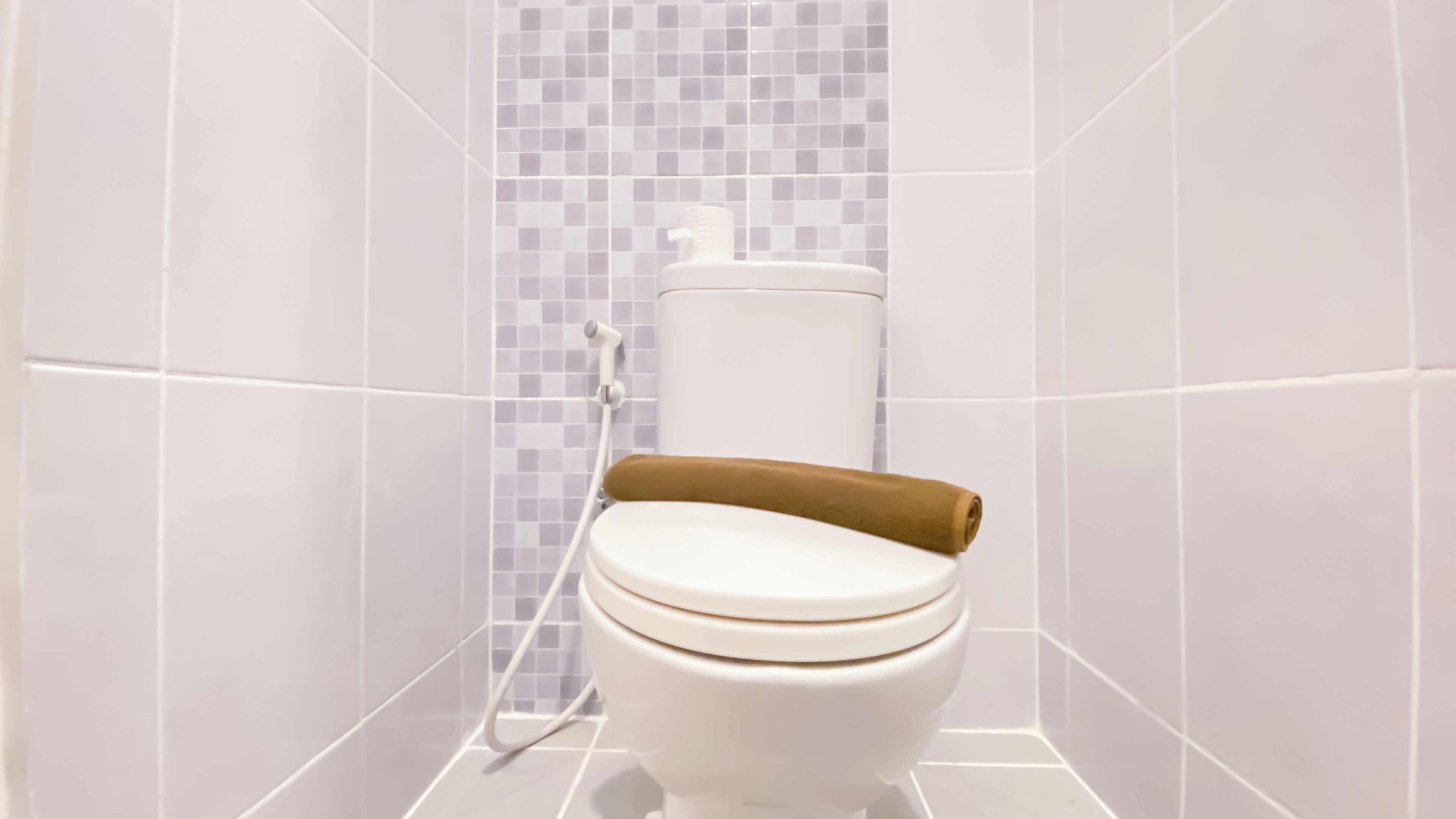 A toilet with a brown towel on the seat, white tiles on the walls, and a white toilet paper holder.