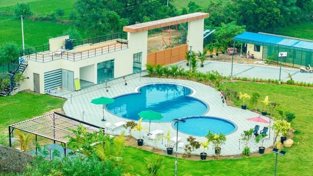 Un edificio moderno con area piscina, comprendente una piscina circolare e una piscina rettangolare separata, circondata da sedute all'aperto e vegetazione.