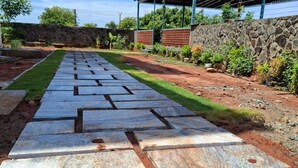Un vialetto lastricato conduce a un padiglione coperto con tetto rosso, circondato da vegetazione e un muro in pietra.