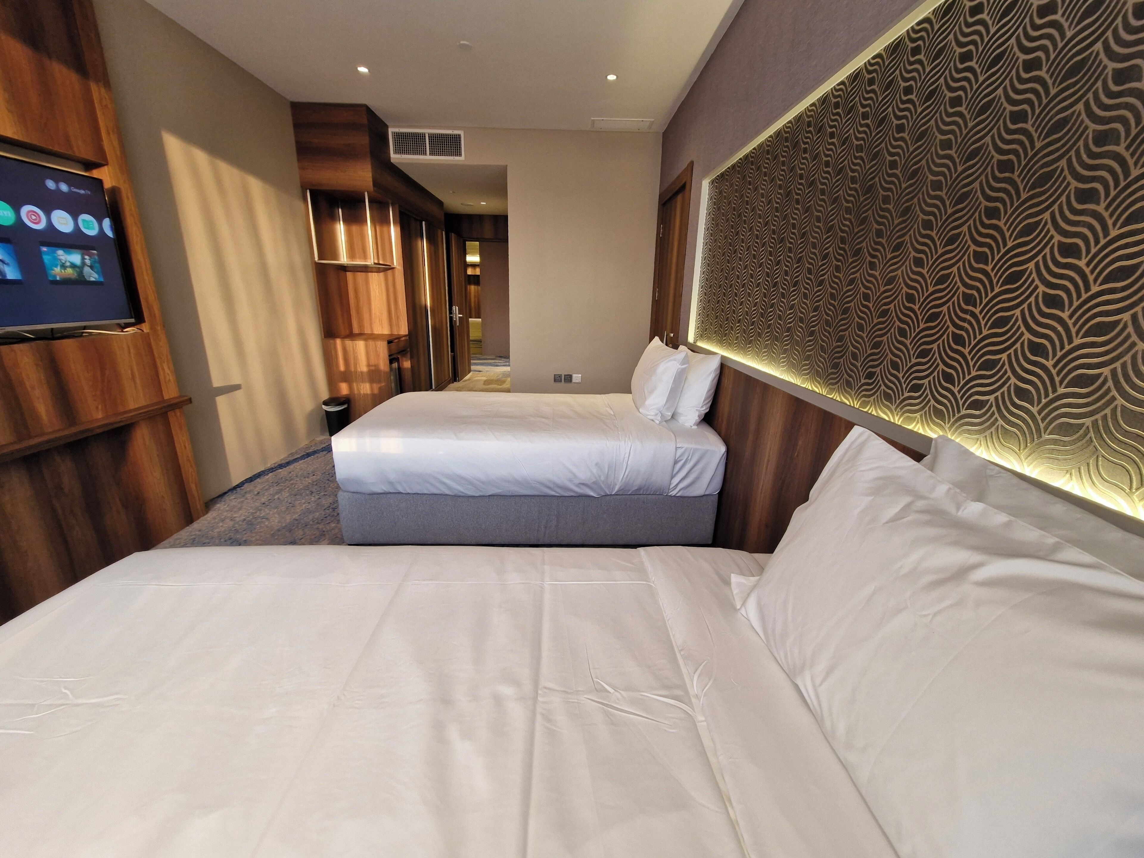 A hotel room with two beds, a TV, wooden paneling, and a patterned headboard.