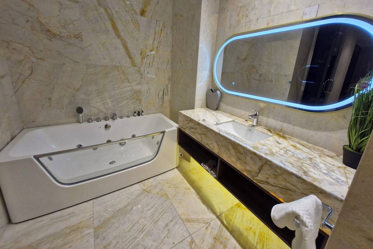 Une salle de bain moderne avec une grande baignoire, un lavabo et un miroir doté d’un cadre éclairé.