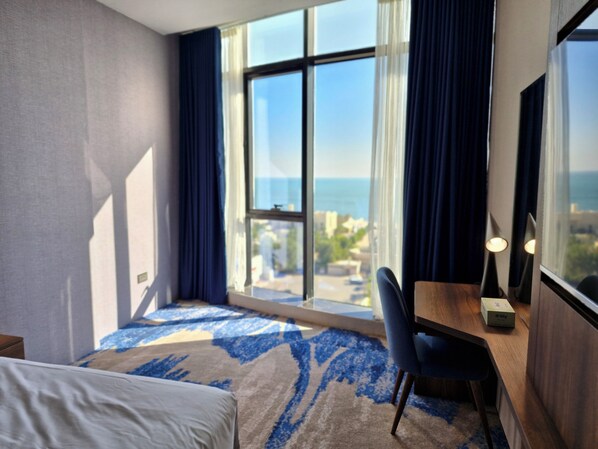 A hotel room with a bed, a desk, and a view of the sea. - Ocean View Hotel Kuwait (Mahboula)
