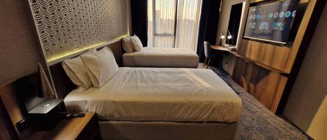 A hotel room with two beds, a desk, a TV, and a patterned headboard.