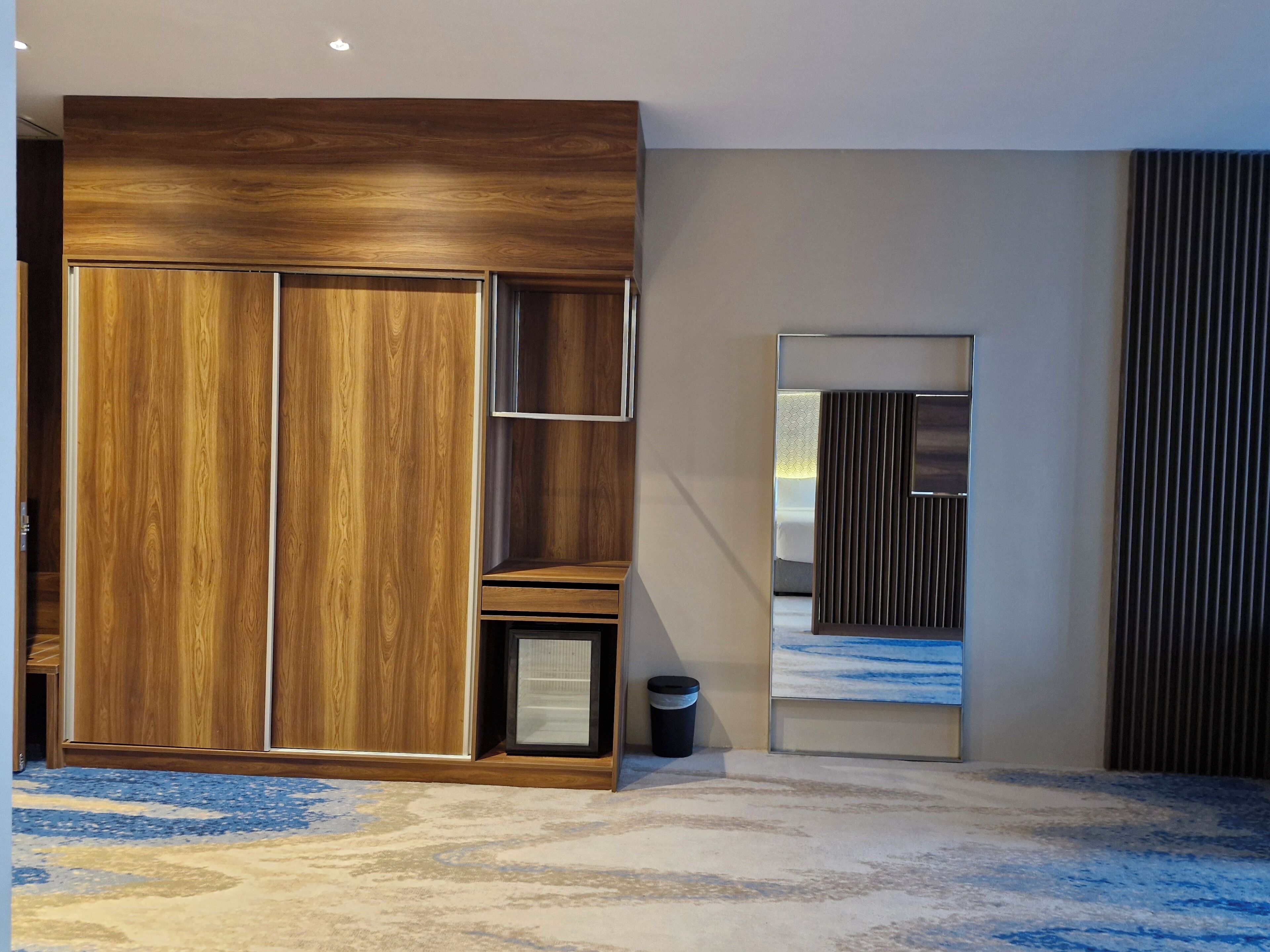 Una habitación moderna con un amplio armario de madera, un pequeño rincón de descanso y un espejo grande.