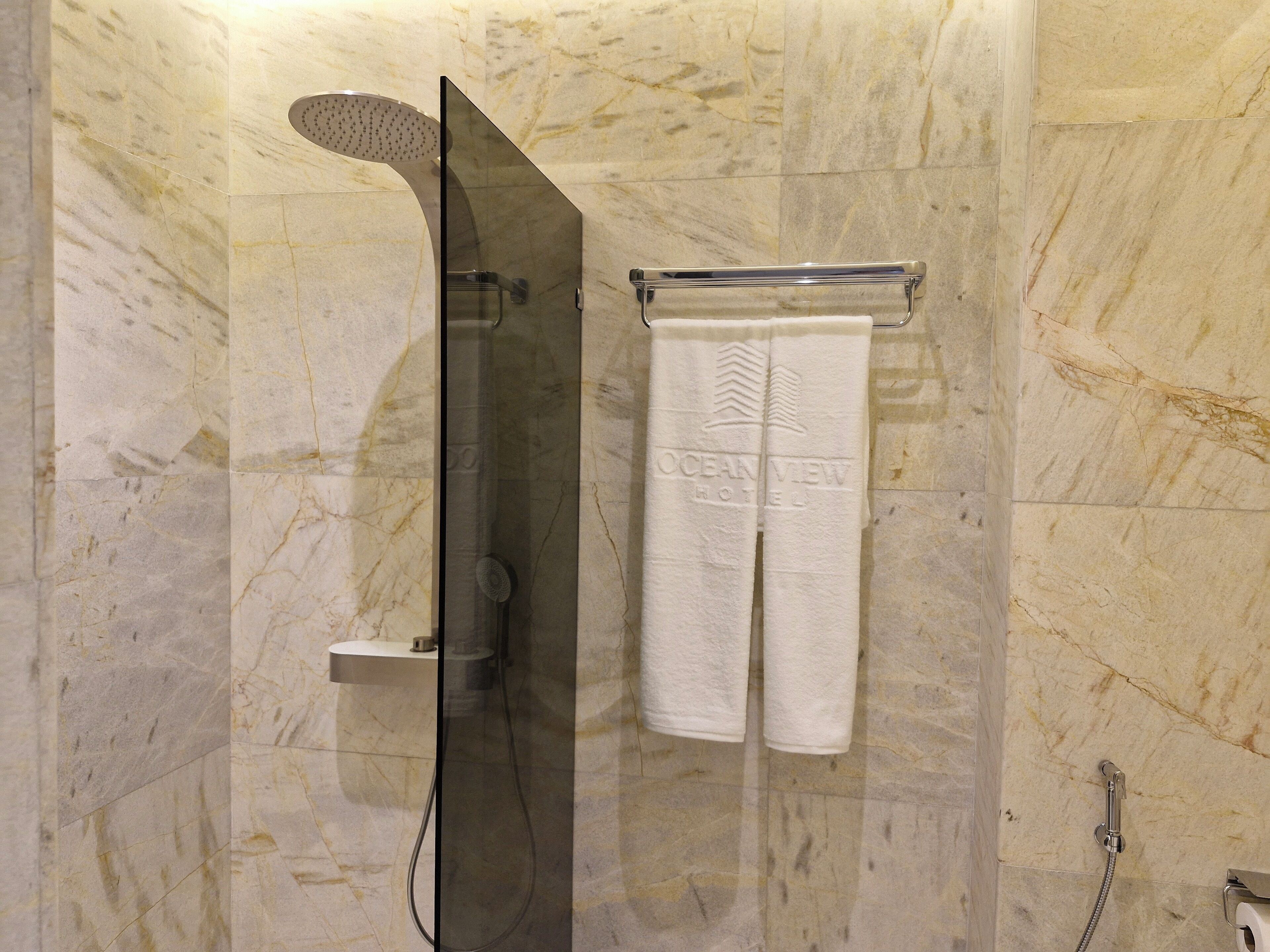 A bathroom with a shower, a towel rack with a towel, and a marble wall.