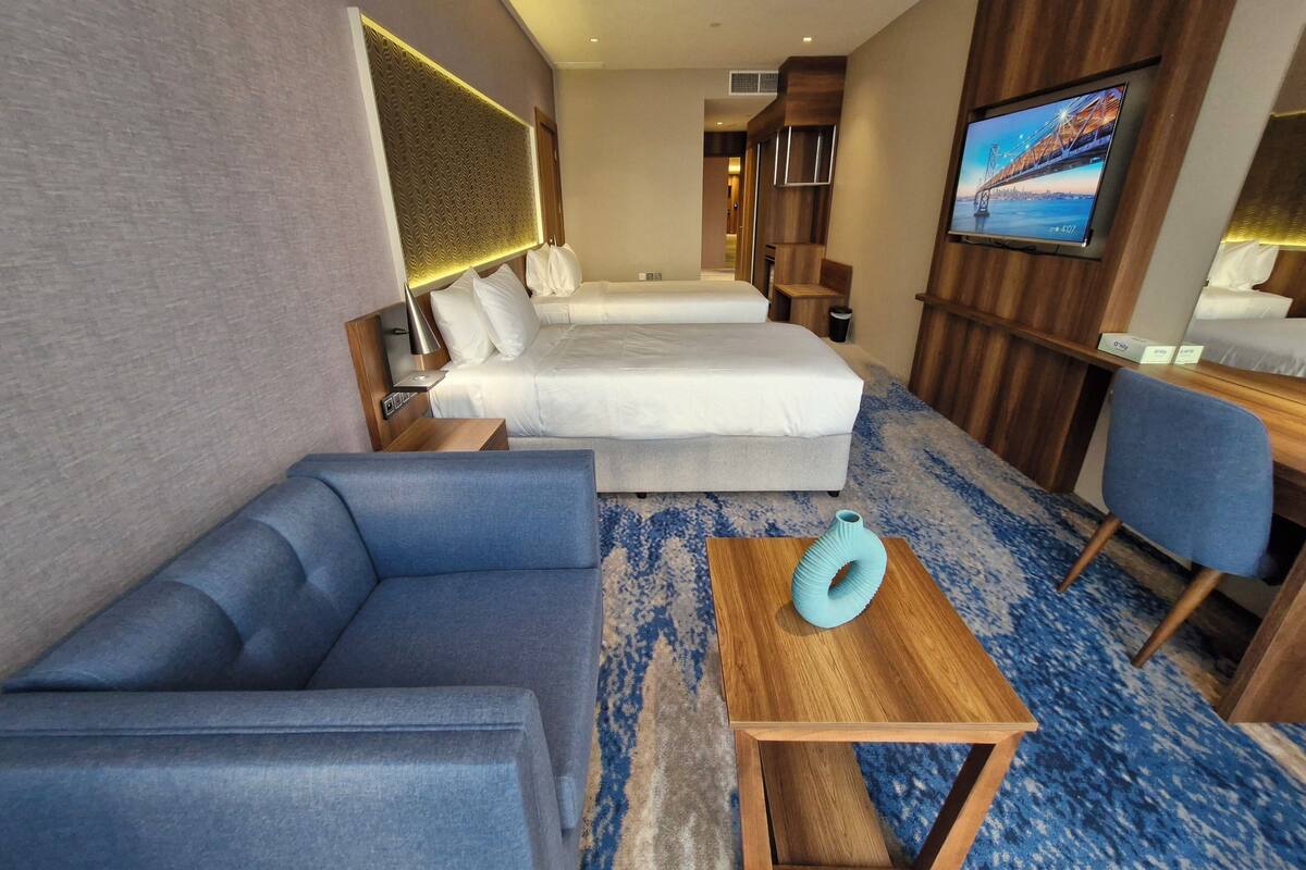 Une chambre d’hôtel avec un canapé, deux lits, une télévision et une table d’appoint en bois.