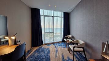 A hotel room with a large window, a desk with a chair, a bed, and a small table.