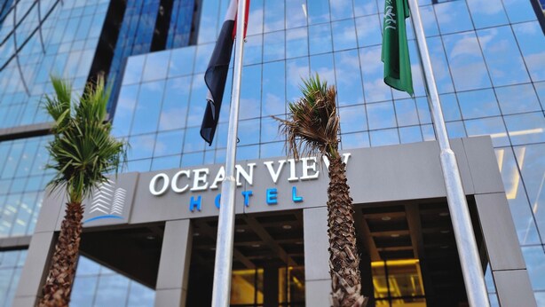 Ocean View Hotel med en moderne glasfacade, palmer foran og flag på stænger.
