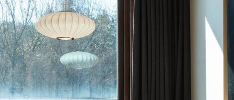 A room with a wooden desk, a chair, a window with curtains, and a hanging light fixture.