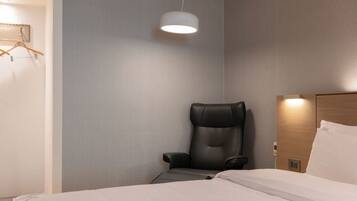 A hotel room with a bed, a black massage chair, a hanging light fixture, and a wooden headboard.