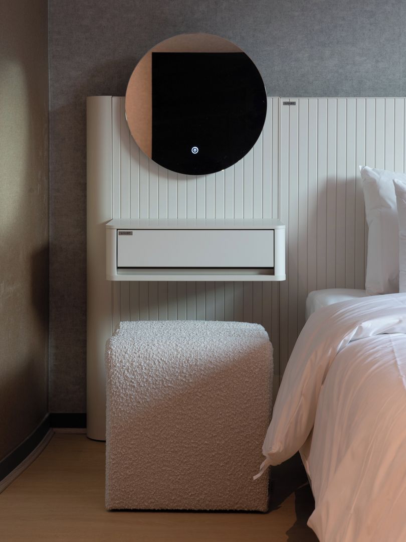 Habitación de hotel moderna con aire acondicionado integrado, una mesita de noche y una cama con ropa blanca.
