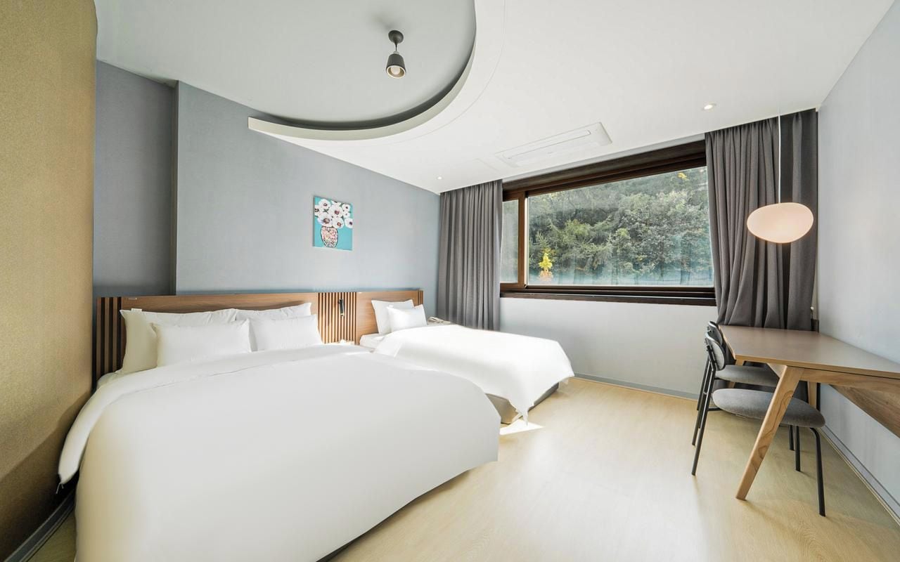 A modern hotel room with a large bed, a desk, and a view of the outdoors.