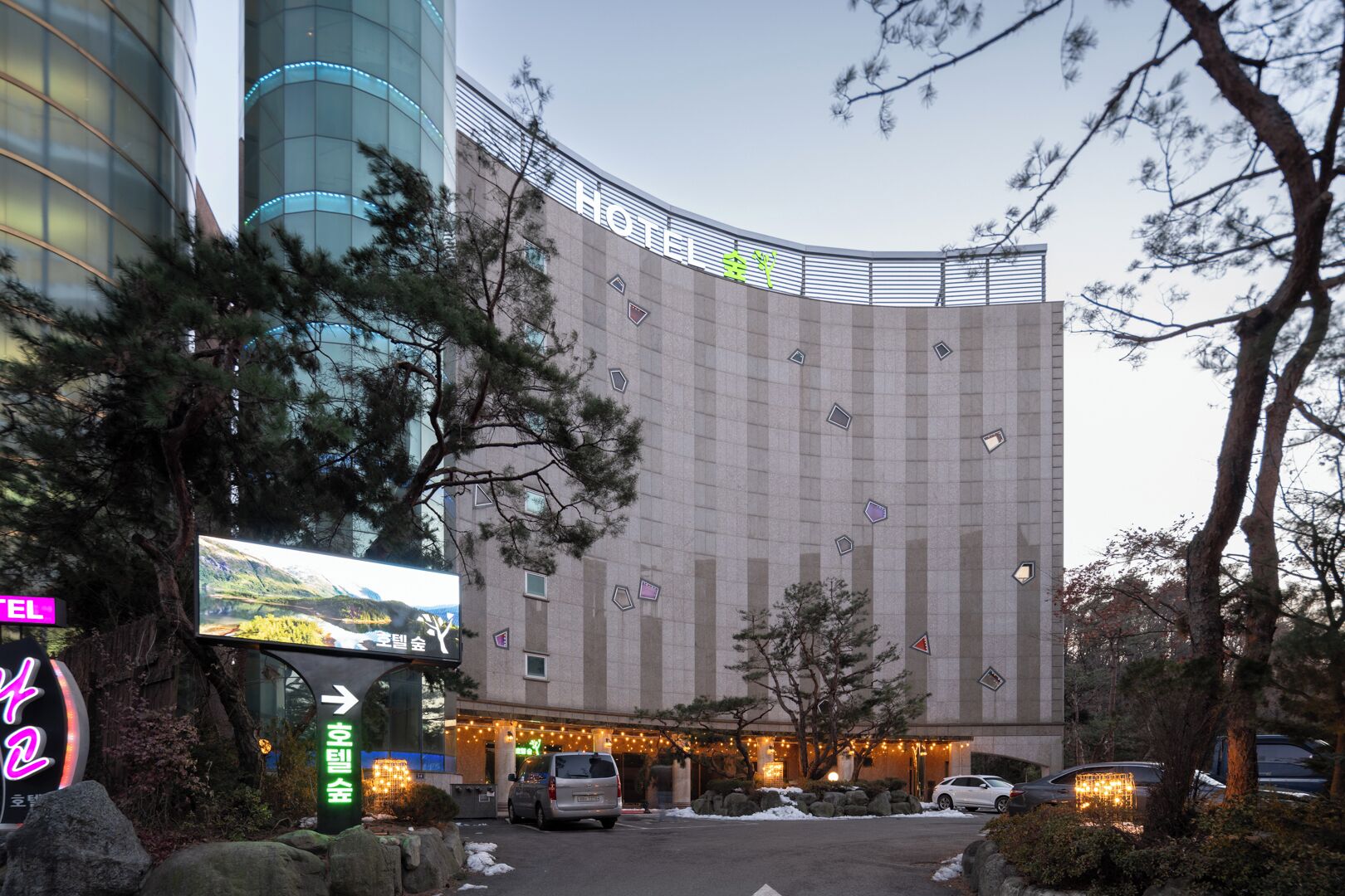 A hotel with a curved facade, large signage, and a parking area with cars.