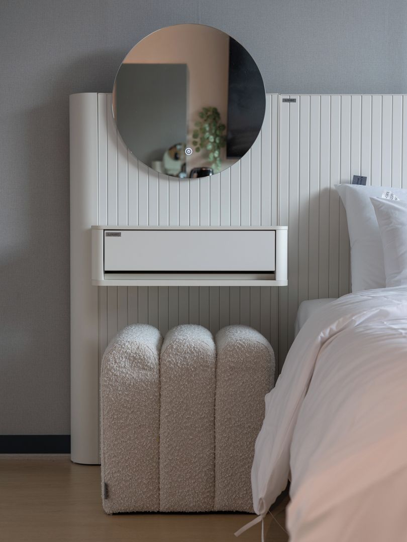 Ein Schlafzimmer mit einem Bett, einem runden Spiegel, einer Wand-Klimaanlage und einem kleinen Hocker.