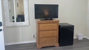 A room with a wooden dresser, a black TV stand, and a white trash bin. - Charming hotel in adorable Lake Wales with WiFi, AC, with a beautiful lake view. (Lake Wales)