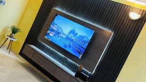 A modern living room with a large flat-screen TV mounted on a dark wall, a ceiling fan, and a small side table with a plant.