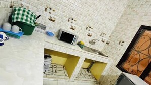 A kitchen with white tiled walls, a yellow countertop, a small refrigerator, and a microwave.