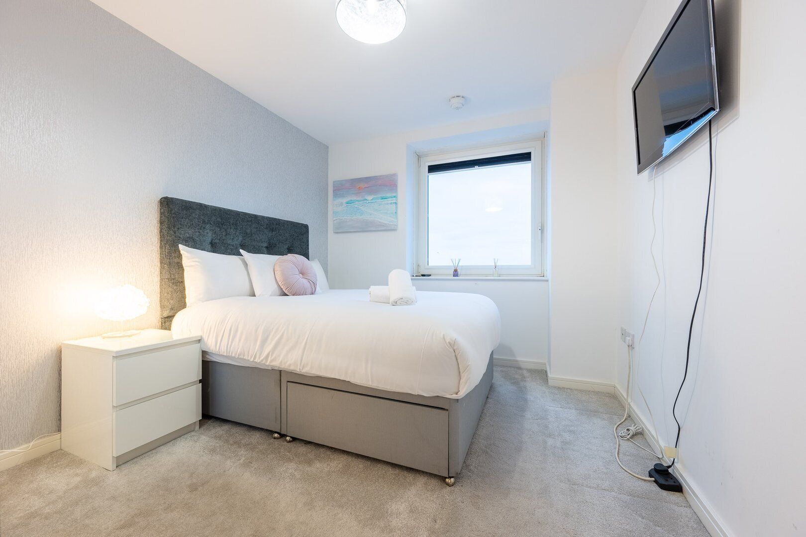 A bedroom with a bed, nightstands, a TV, and a window.
