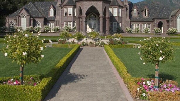 A large, stately mansion with a symmetrical facade, a central entrance, and a formal garden with manicured hedges and flowering plants. - Villa Colibri, by Vinifera Homes (Kenwood)