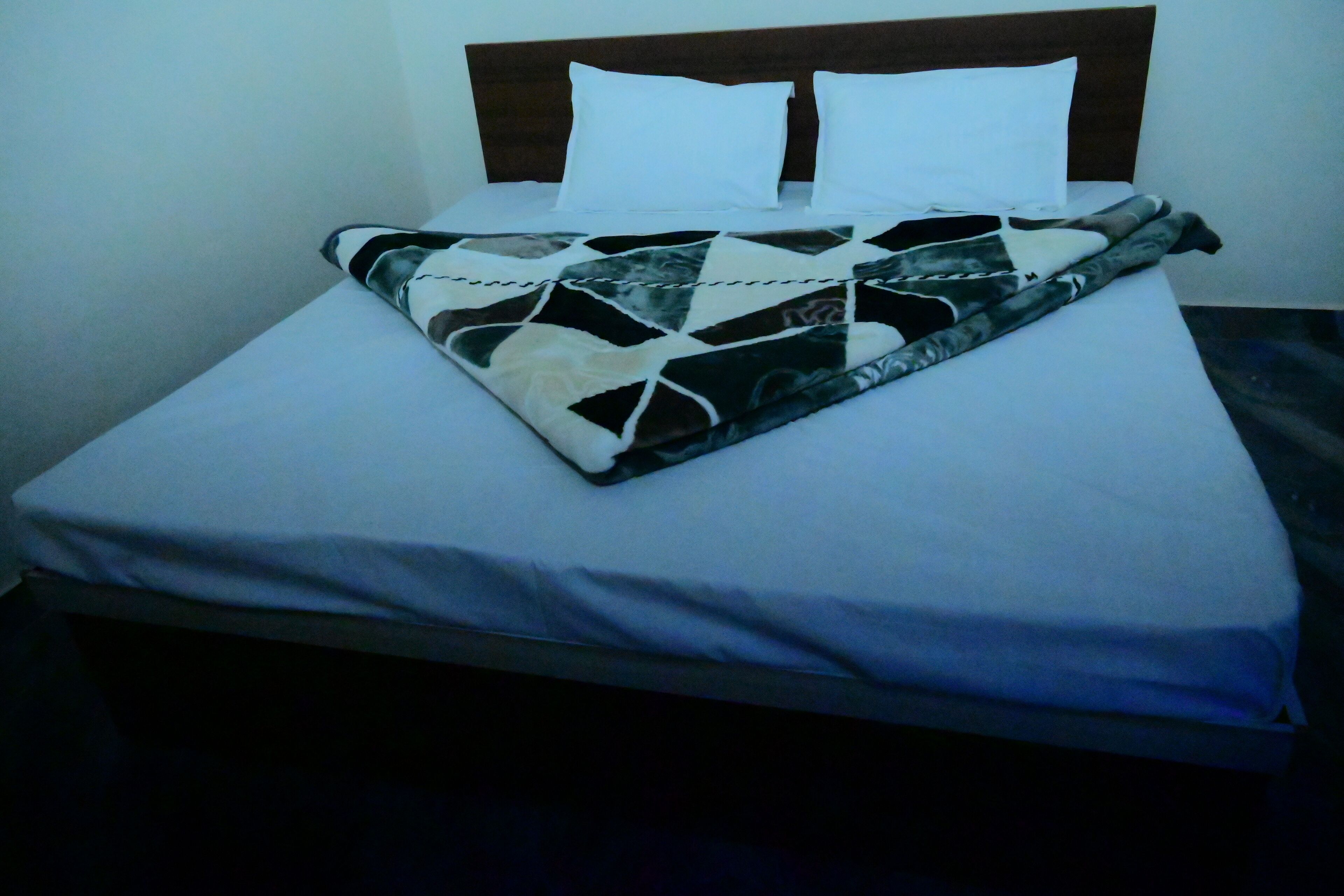 A bed with a patterned blanket, white pillows, and a wooden headboard.
