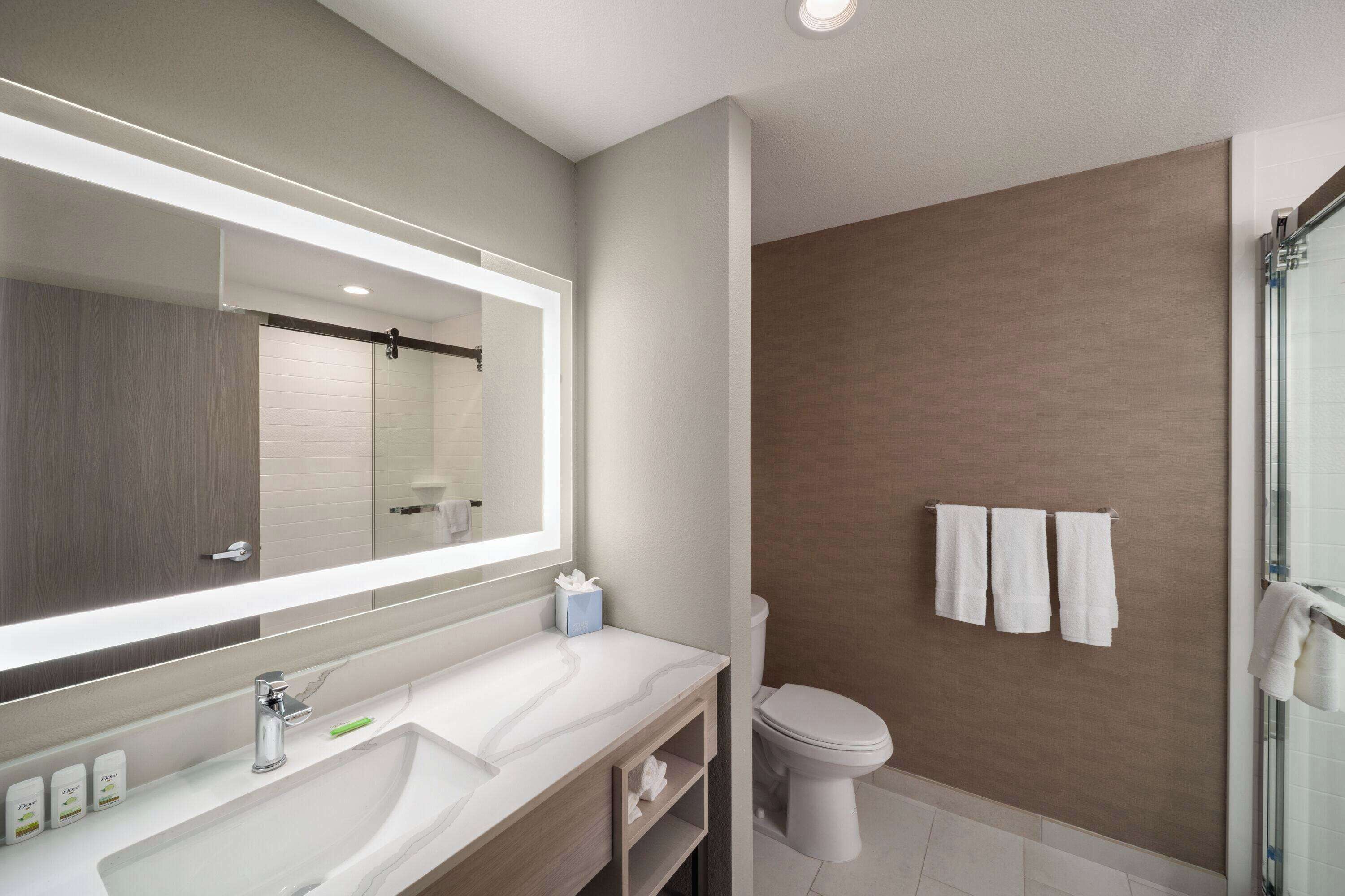 Un baño moderno con un espejo grande, dos lavamanos, un inodoro y una cabina de ducha de cristal.
