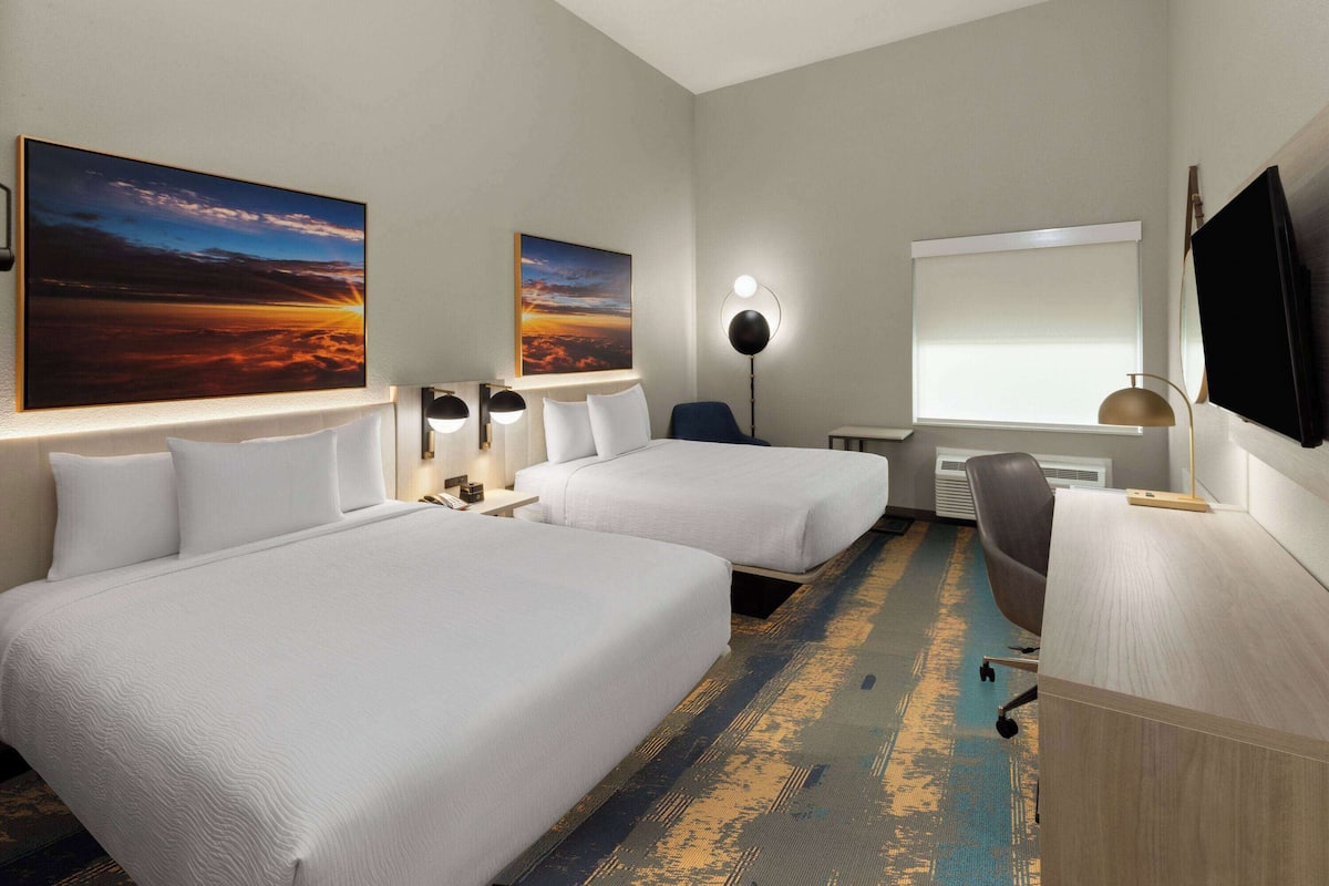 Une chambre d’hôtel avec deux lits, un bureau, une chaise, une télévision et des œuvres d’art accrochées aux murs.