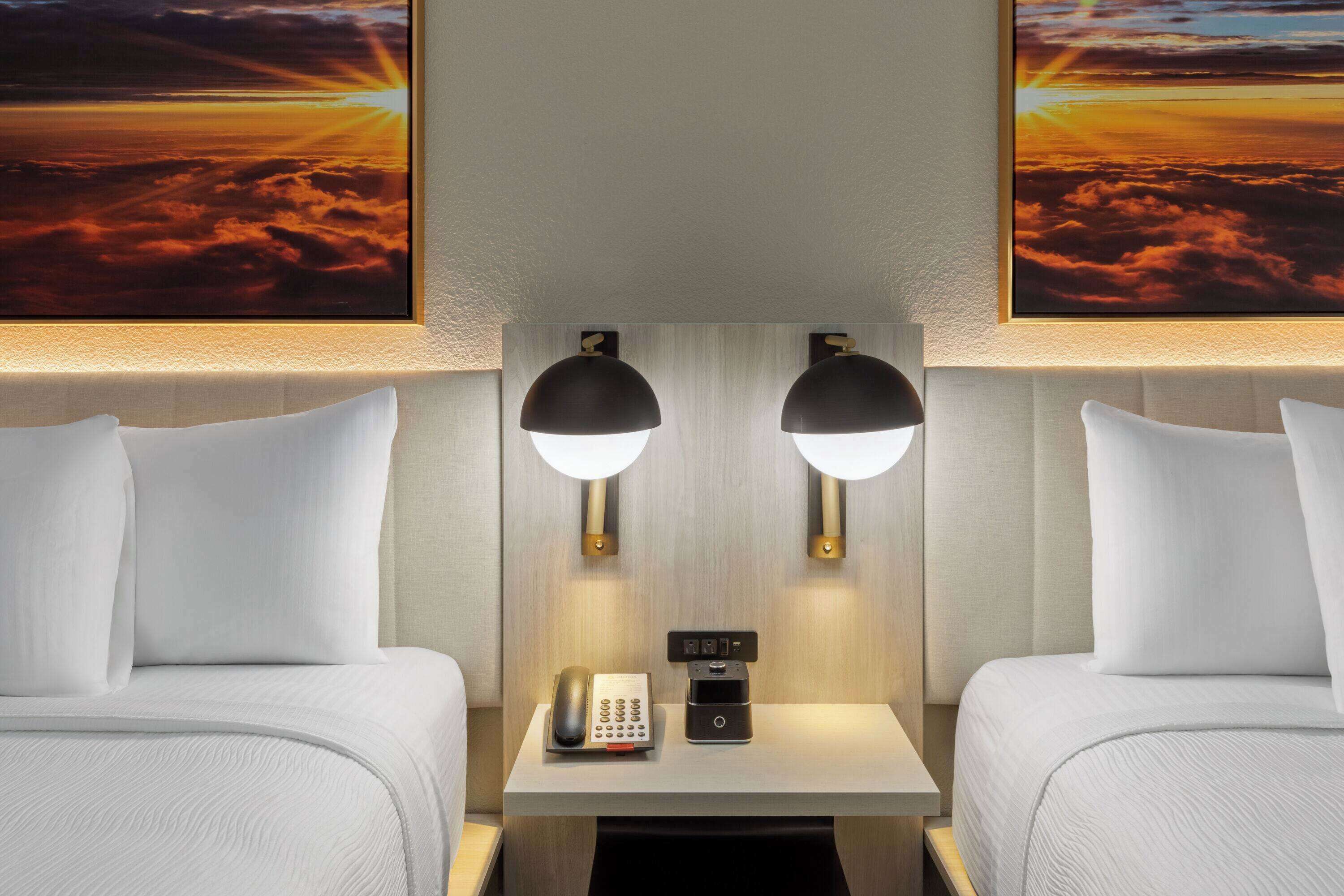 Une chambre d’hôtel avec deux lits, une table de chevet avec un téléphone et une machine à café, et des lampes fixées au mur.