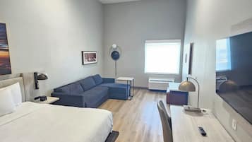 A modern hotel room with a bed, a sofa, a desk, and a TV.