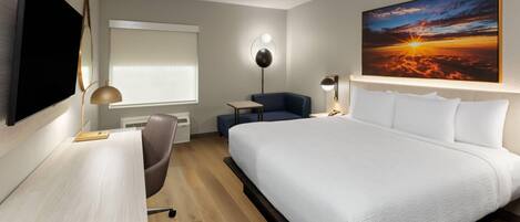 A modern hotel room with a large bed, a desk, a chair, a small table, and a TV.