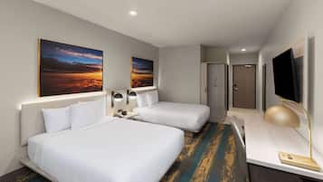 Habitación de hotel con dos camas, un escritorio con lámpara, televisor y dos cuadros en la pared.