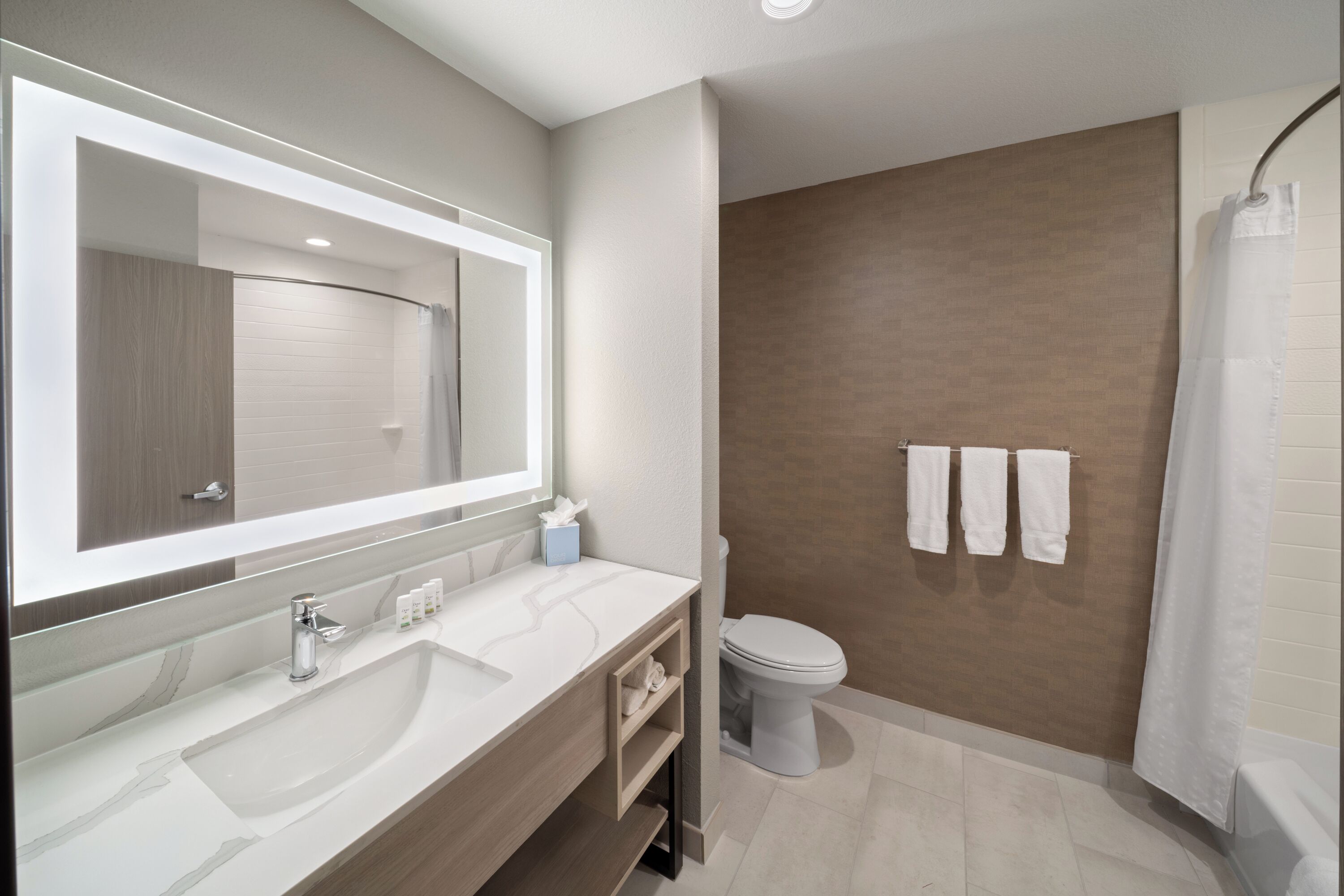 A modern bathroom with a large mirror, a sink, a toilet, and a shower area.