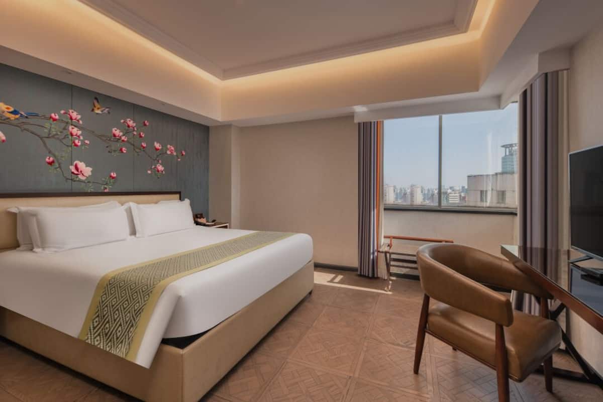 Een hotelkamer met een groot bed, een stoel, een televisie en uitzicht over de stad.