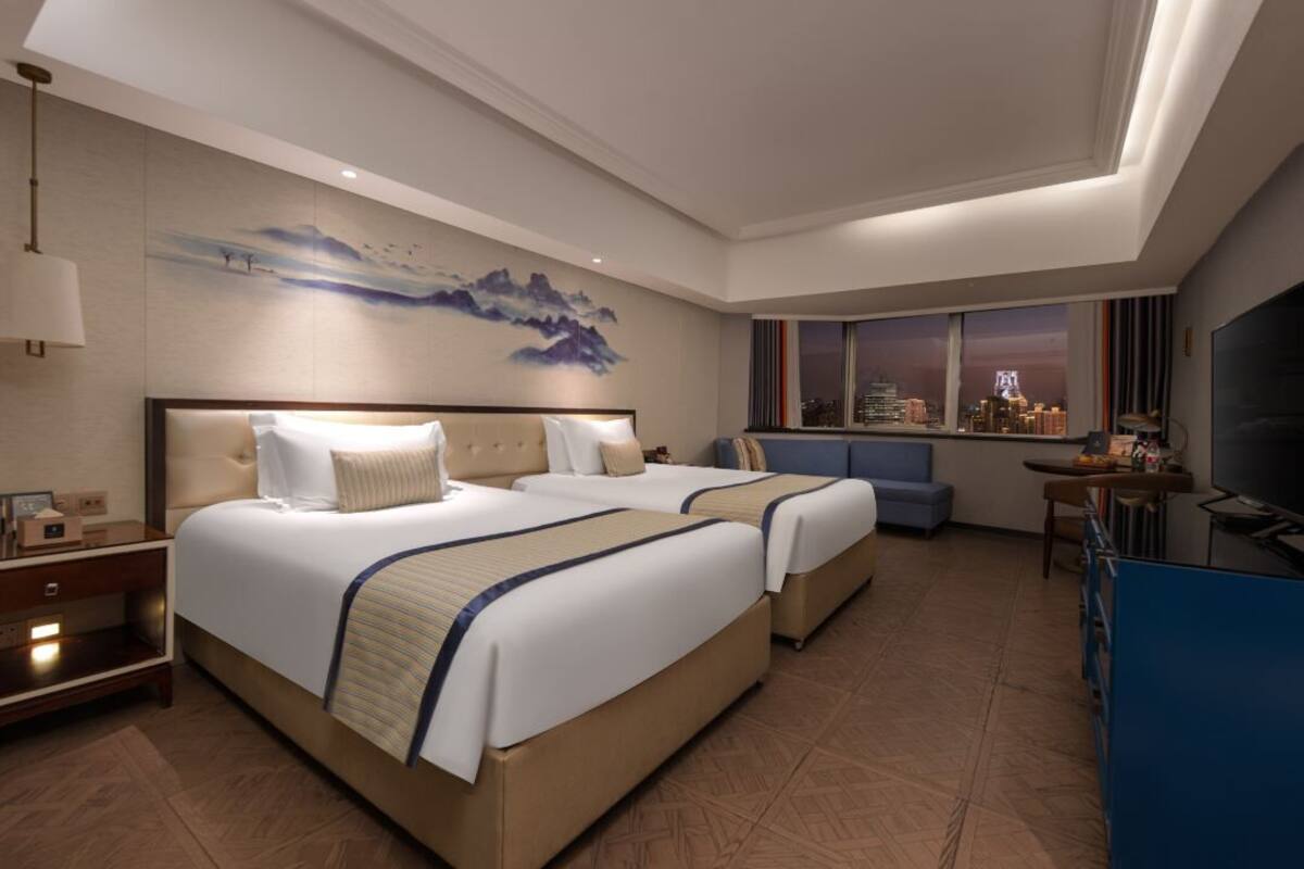 Een hotelkamer met twee bedden, uitzicht op de stad, een bureau en een televisie.