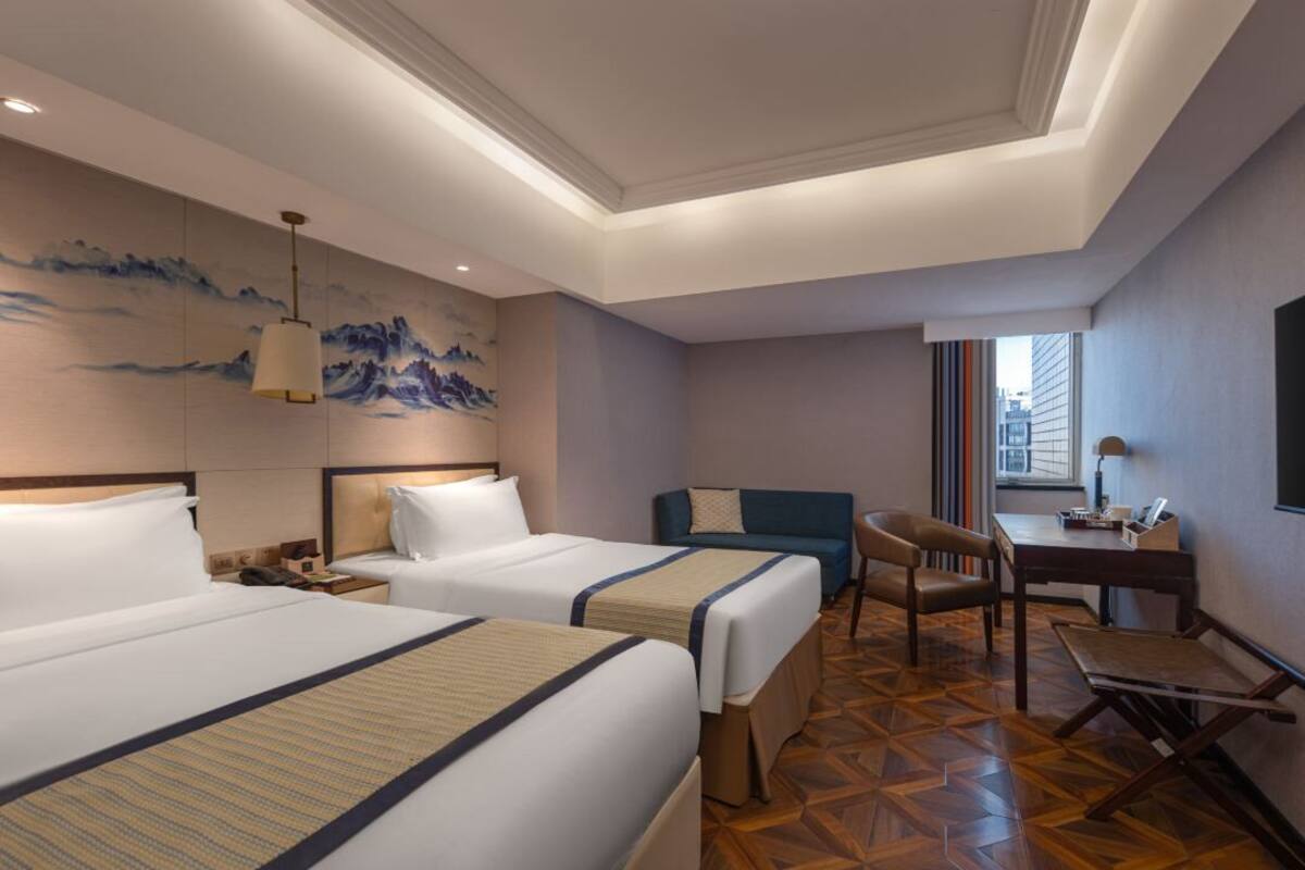 Een hotelkamer met twee bedden, een bureau, een stoel en uitzicht op de stad.